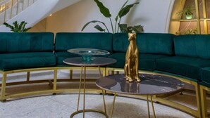 Un intérieur moderne avec un escalier à volutes, des sièges recouverts d’un tissu vert et une statue dorée.