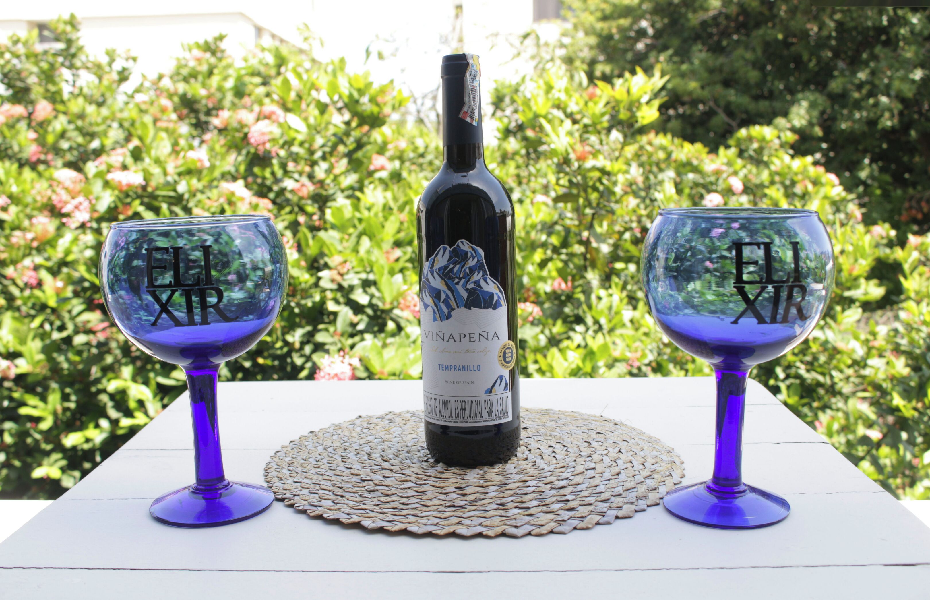 Een fles wijn op een tafel met twee glaasjes, elk met de tekst 'EL VINO'.