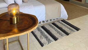 Un dormitorio con una cama grande, una araña de cristal, una mesa de madera y vistas a un jardín de cactus por una ventana abierta.