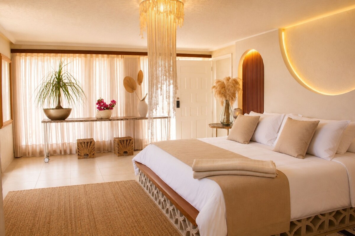 Une chambre à coucher moderne avec un grand lit, une table de chevet ornée d’un vase et un luminaire suspendu.