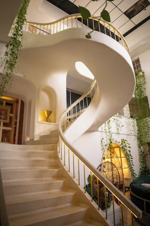 A spiral staircase with a white railing, surrounded by greenery and a lamp. - Casa Elixir Boutique  (Barranquilla)