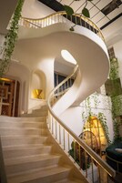 Una escalera en espiral con barandilla blanca, rodeada de follaje y una lámpara.