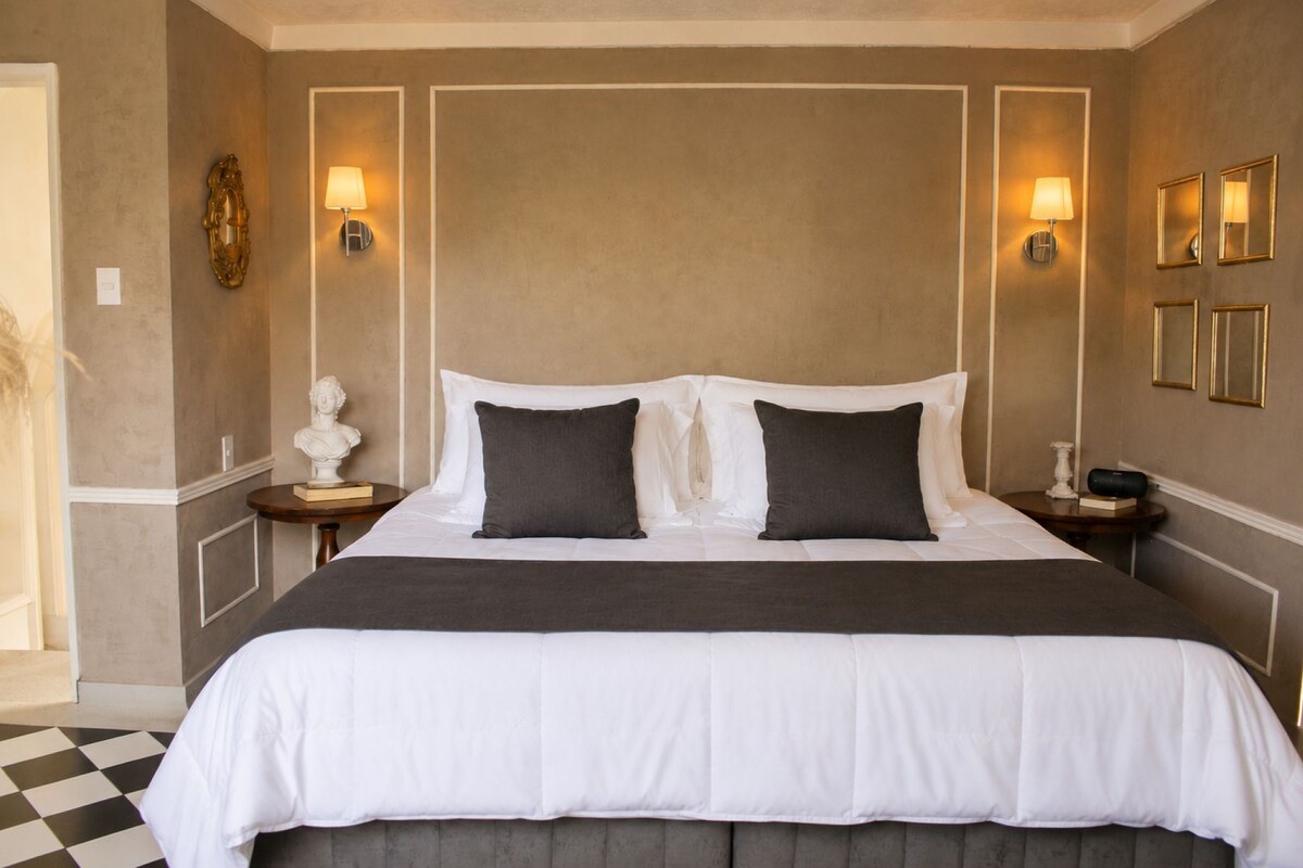 A hotel room with a large bed, two bedside tables, and wall-mounted lamps.