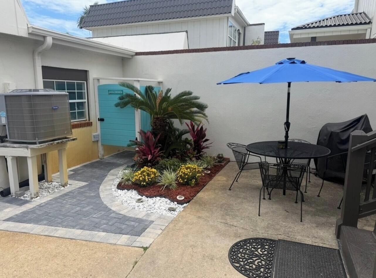 A patio with a table and chairs, a blue umbrella, and a small garden with various plants.