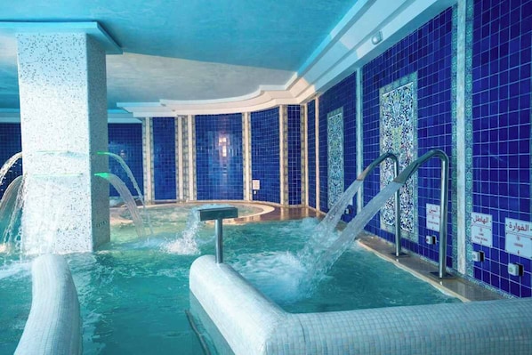 Un espace de bien-être comprenant un jacuzzi, des jets d’eau et des murs recouverts de carreaux bleus.