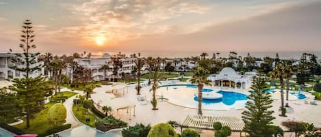 A resort with multiple swimming pools, a landscaped garden, and a view of the ocean at sunset.