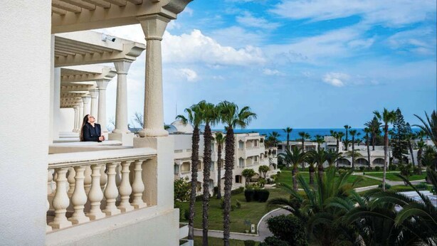 Un hôtel doté d’un balcon, de palmiers et offrant une vue sur la mer.