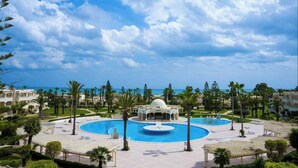 Un complexe hôtelier doté d’une grande piscine centrale, de palmiers et offrant une vue sur la mer.