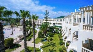 Une cour intérieure agrémentée de palmiers, une piscine et un bâtiment blanc doté de balcons.