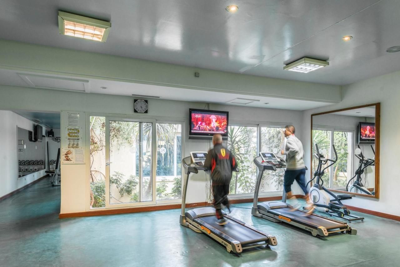 Un gimnasio con cintas de correr, televisión y ventanas amplias.