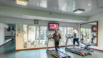 Un gimnasio con cintas de correr, televisión y ventanas amplias.