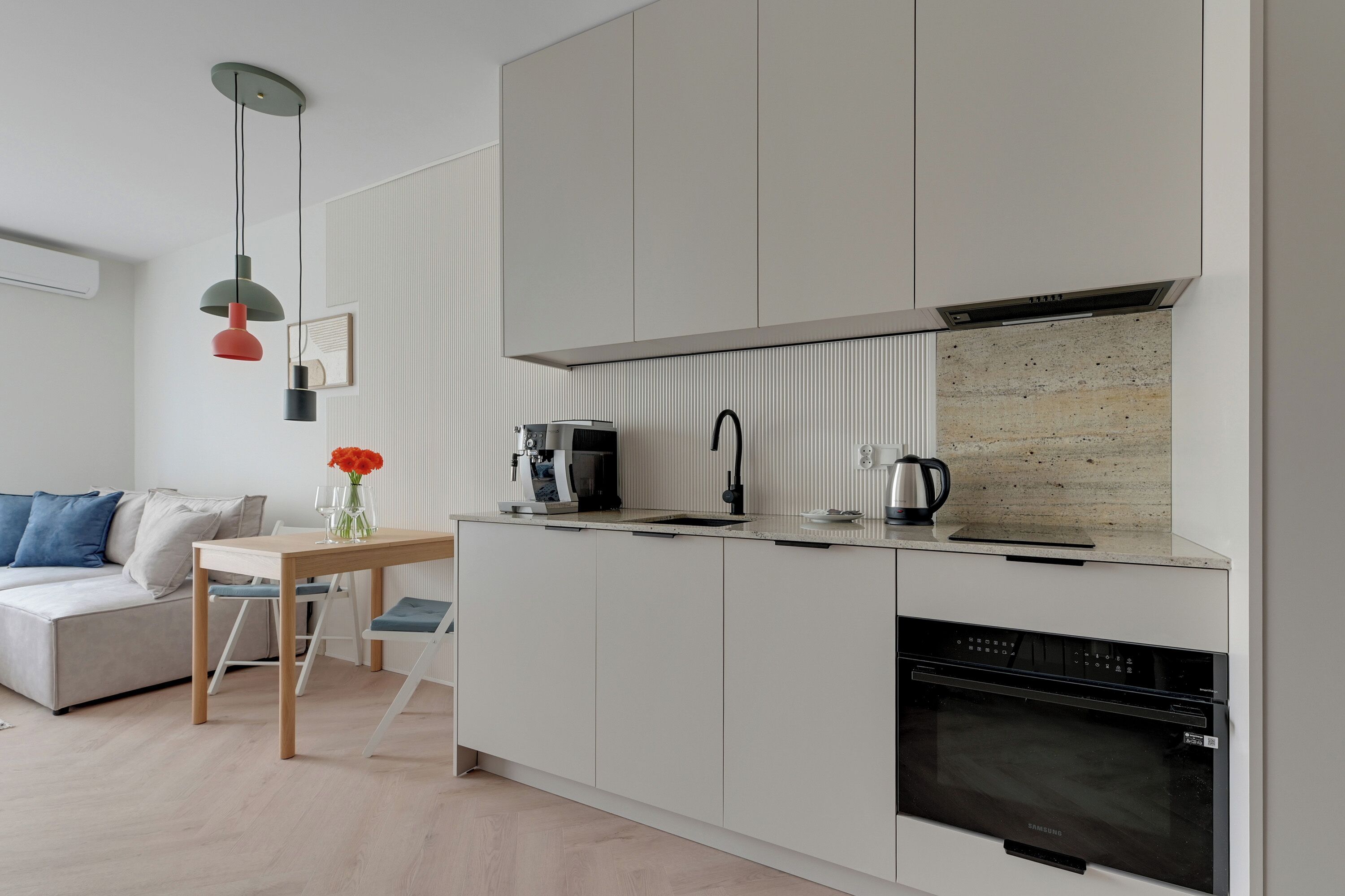 A modern kitchen with a built-in oven, a coffee maker, and a kettle on the countertop.
