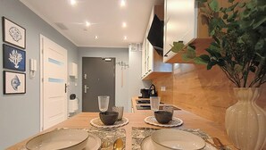 Ein Essbereich mit einem Holztisch, gedeckt für vier Personen, einer Kaffeemaschine und einem an der Wand befestigten Fernseher.