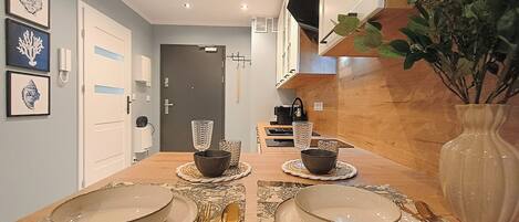 A dining area with a wooden table set for four, a coffee machine, and a TV mounted on the wall.