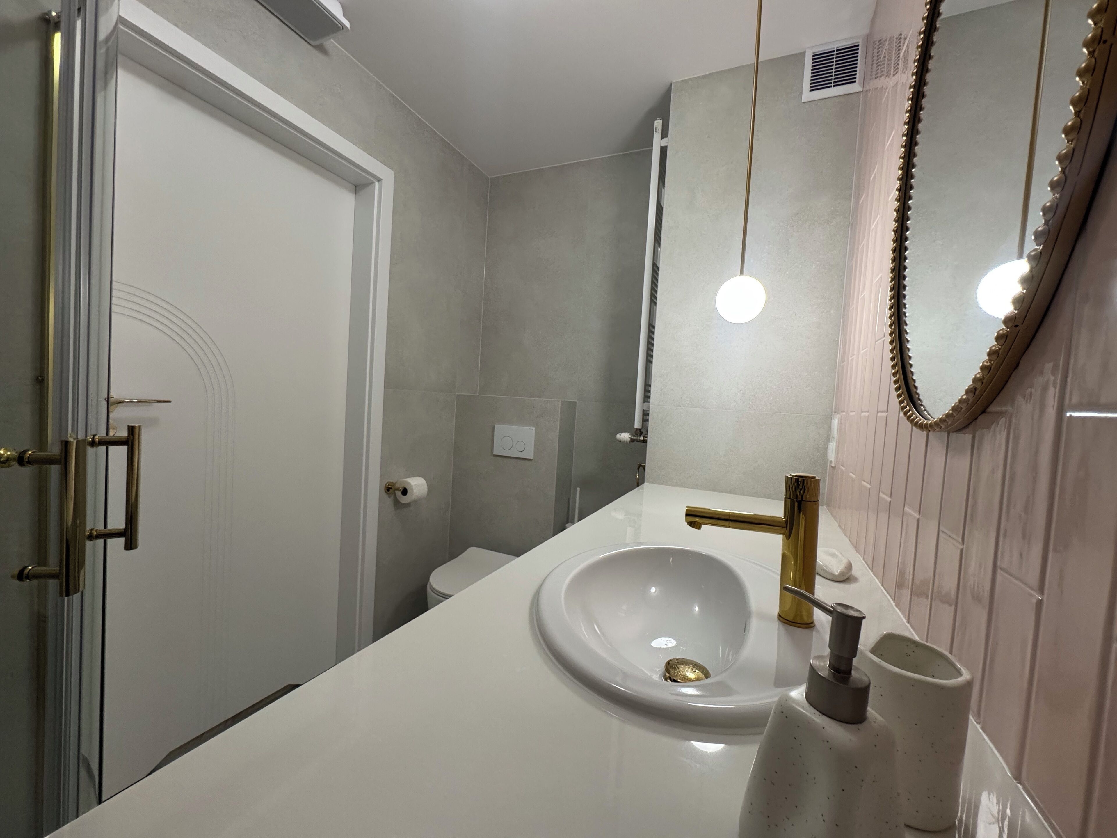 A modern bathroom with a white sink, gold faucet, and a large mirror with a decorative frame.