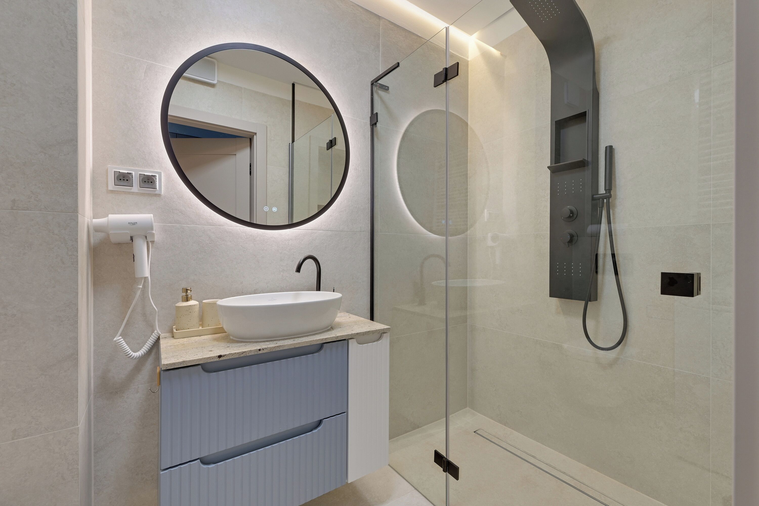 A modern bathroom with a round mirror, a sink, a glass-enclosed shower, and a towel rack.