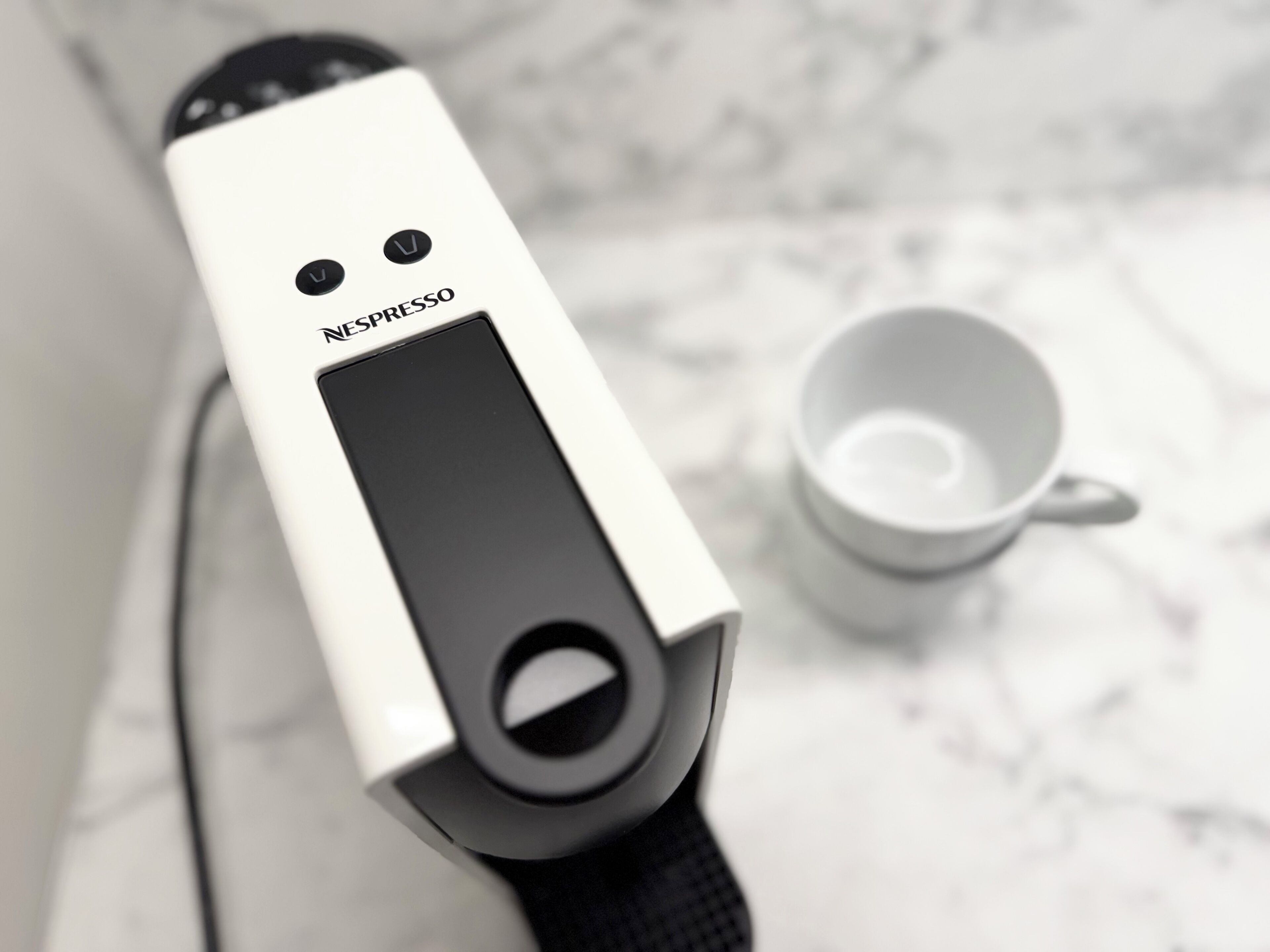 Eine Nespresso-Kaffeemaschine mit Schwarz-Weiß-Design, eine Kaffeetasse und eine weiße Tasse auf einer Marmorplatte.