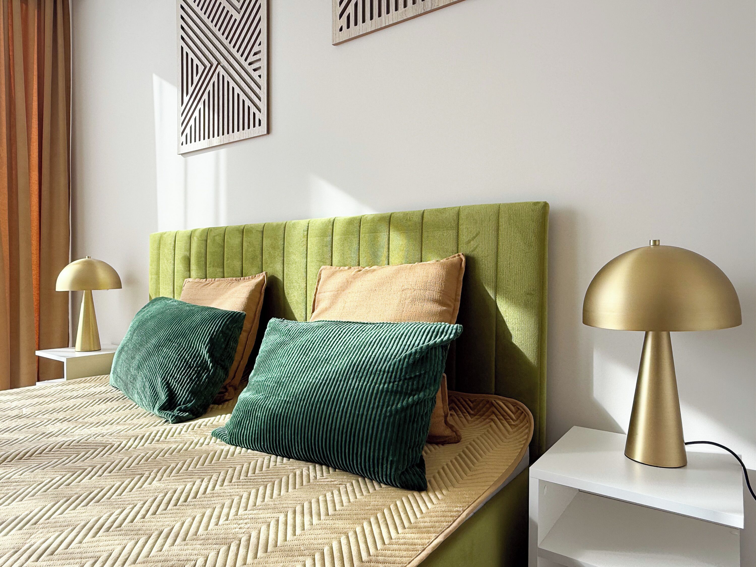 A neatly arranged bedroom with a green upholstered headboard, two bedside lamps, and a patterned bedspread.
