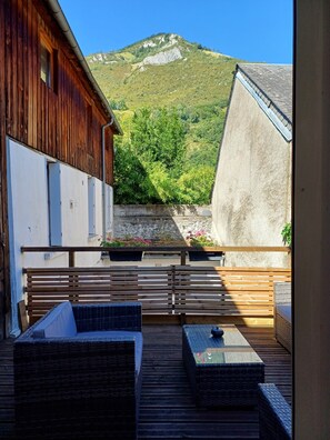 Une terrasse en bois avec des meubles en osier, une vue sur une montagne et un bâtiment doté d’un toit en pente.