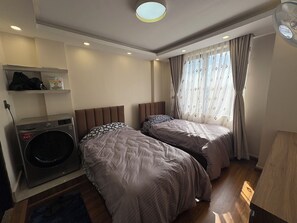 Una camera d'albergo con due letti, una lavatrice, un ventilatore a soffitto e una finestra con tende.