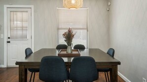 Een eetkamer met een houten tafel, vier stoelen, een vaas met gedroogde bloemen en een hanglamp.