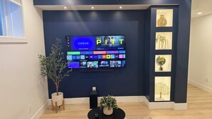 A modern living room with a large flat-screen TV mounted on a dark blue wall, surrounded by decorative items including a vase, a sculpture, and a globe. - Modern 1BR Private Suite Near Airport and Amazing Shopping!Free Netflix, Parking (Calgary)