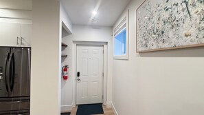 Un passadís amb una porta blanca, un extintor, un frigorífic d'acer inoxidable i una obra d'art emmarcada a la paret.