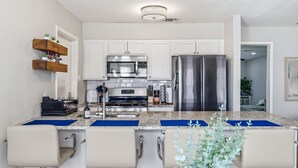 Une cuisine moderne avec des meubles blancs, des appareils en acier inoxydable et un coin bar équipé de tabourets.