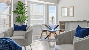 Un salon moderne avec une table à manger ronde, des canapés gris et une grande plante en pot.