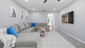 Un salon moderne avec un canapé d’angle, une table basse et un téléviseur à écran plat fixé au mur.