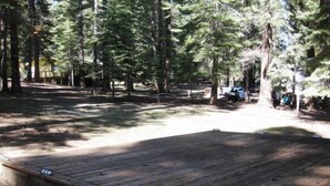 A wooden deck with a ramp leading up to a covered area, surrounded by trees. - Droge-Yuklois, LACC in Lake Almanor, CA (Lake Almanor)