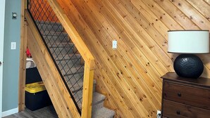 A room with a wooden sloped ceiling, a staircase with a metal railing, a lamp on a dresser, and a trash bin. - Lakeside Retreat in Chester, CA (Chester)