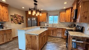 A spacious kitchen with wooden cabinets, a large island, and a herringbone floor pattern. - 20 minutes to Monarch w/ Hot Tub & Game Room! (Salida)
