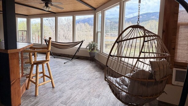 A room with a wooden ceiling, large windows, a hanging chair, a hammock, and a hanging egg chair. - 20 minutes to Monarch w/ Hot Tub & Game Room! (Salida)