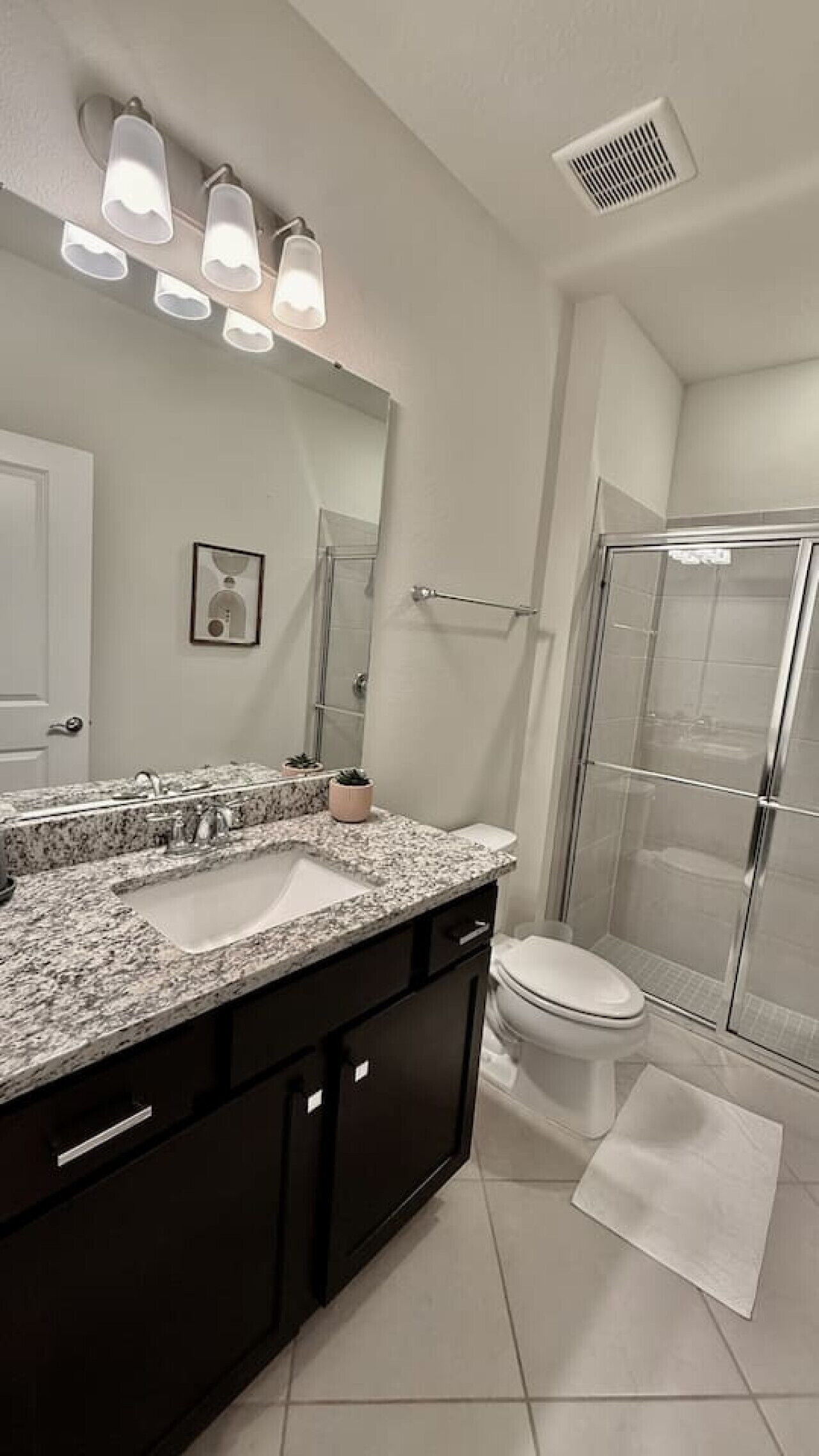 A modern bathroom with a double sink vanity, a large mirror, a toilet, and a glass-enclosed shower.