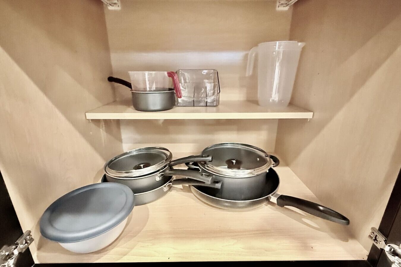 Ett kök med hyllor i trä där kastruller, stekpannor och plastbehållare förvaras.