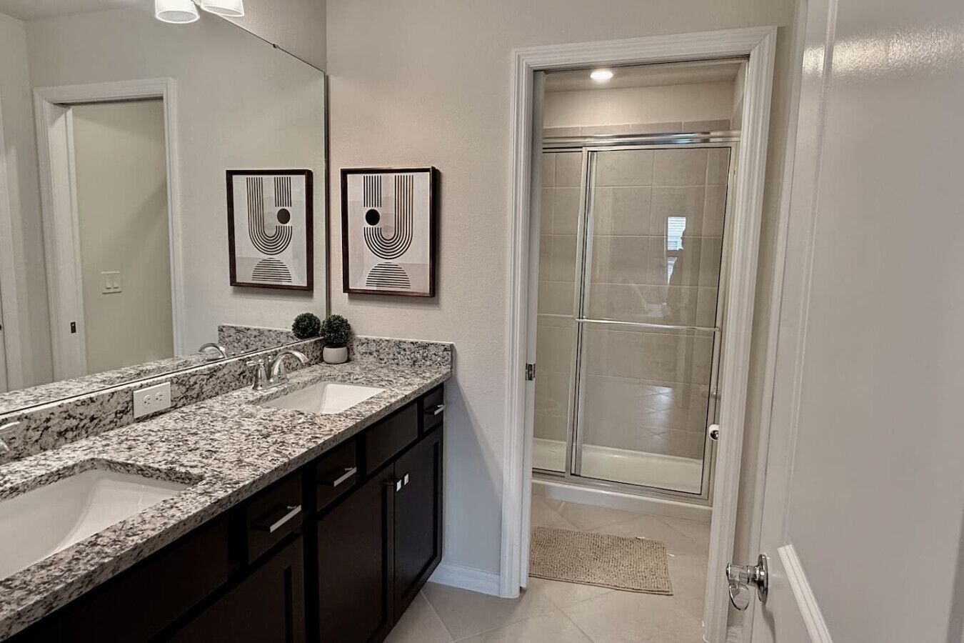 A bathroom with a double sink vanity, a shower enclosure, and two framed wall art pieces.