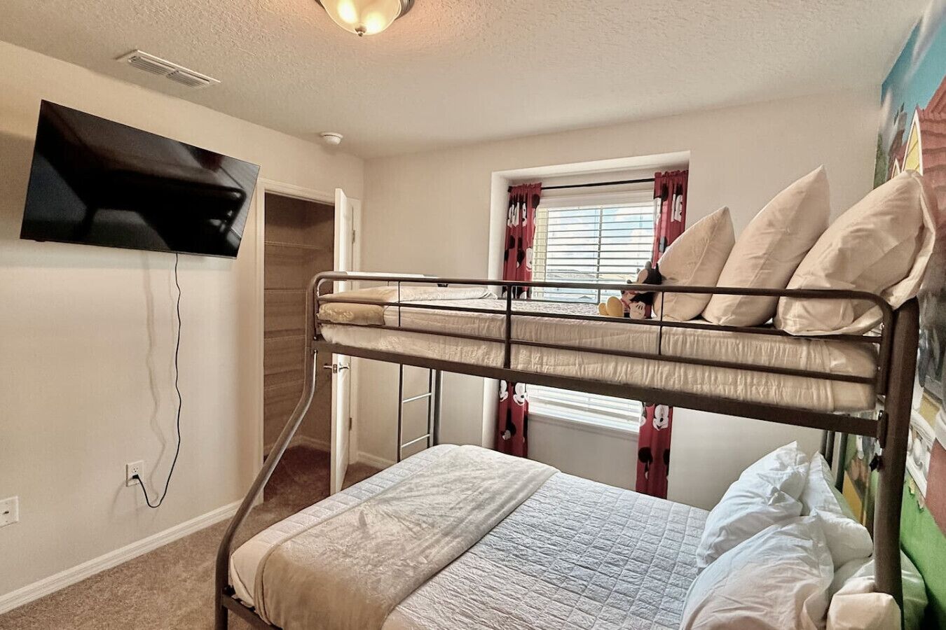 Habitación con literas, una televisión montada en la pared, una ventana con cortinas y una puerta que da a otra habitación.