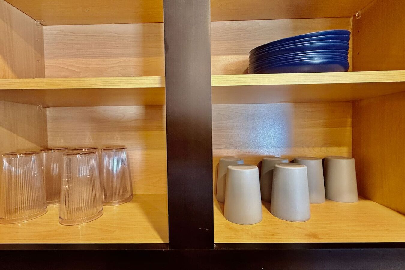 Una estantería de madera con vasos de vidrio transparente y vasos grises.