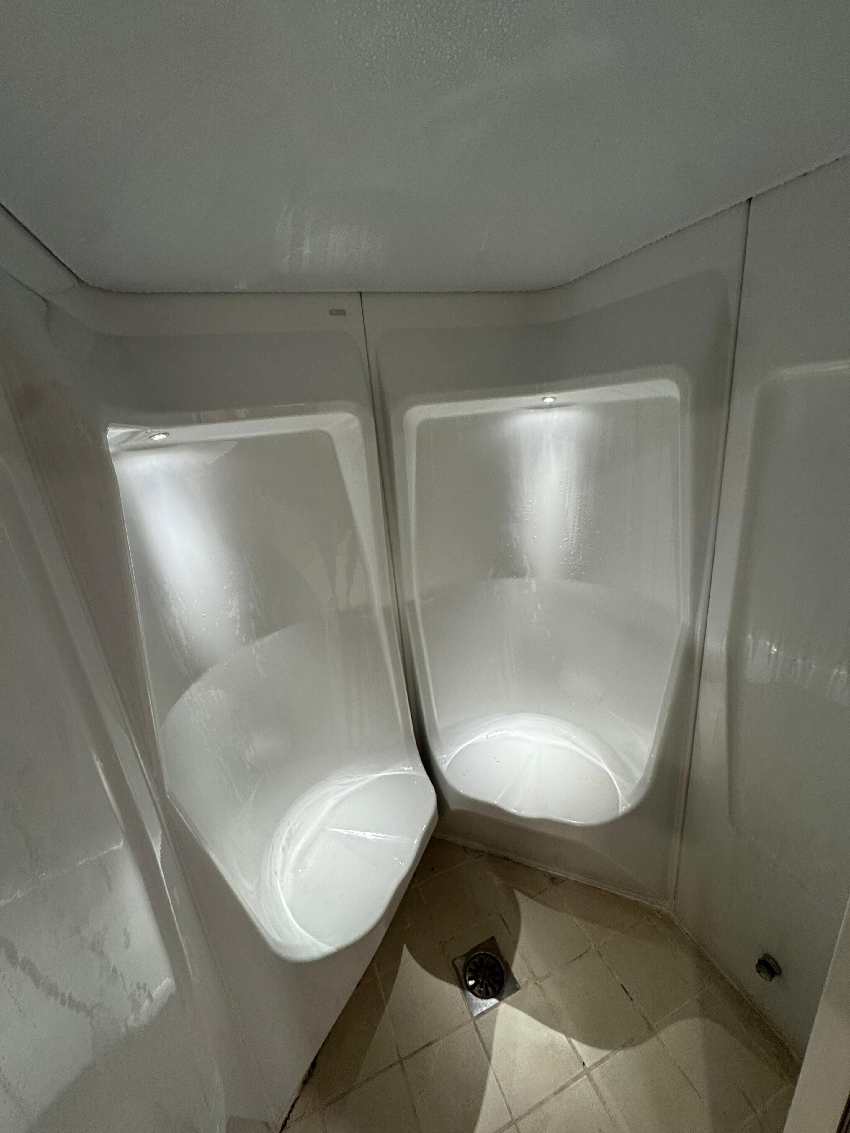 Een toilet met twee urinoirs en een vloerafvoer.