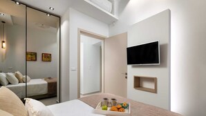 Ein modernes Schlafzimmer mit einem Bett, einem Fernseher, einer Ablage mit Snacks und einem Spiegel.
