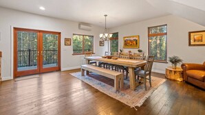 Un espace repas avec une table en bois, des bancs et des chaises. Deux portes-fenêtres coulissantes donnent sur un balcon doté d’une balustrade.