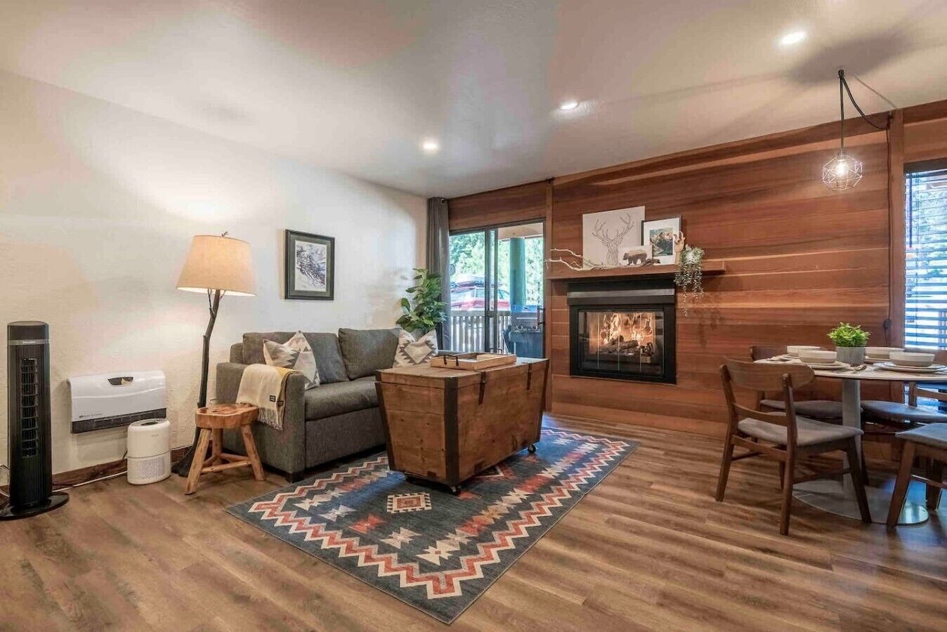 A living room with a fireplace, wooden walls, a sofa, a coffee table, and a dining area.