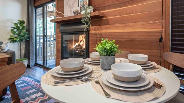 A dining area with a round table set for four, surrounded by wooden walls and a fireplace. - Kings Beach Studio • Pool, Hot Tub, SUP, & Sauna • Kings Beach & Northstar (Tahoe Vista)
