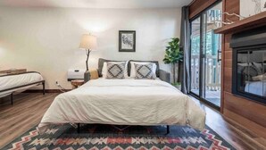 A bedroom with a bed, bedside table, lamp, and a window with a view. - Kings Beach Studio • Pool, Hot Tub, SUP, & Sauna • Kings Beach & Northstar (Tahoe Vista)