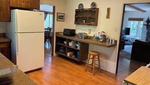 A compact kitchen with a refrigerator, microwave, and a small island with stools. - The Emerald Lake House (Lake Almanor)