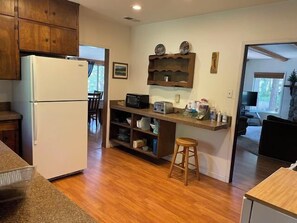 A compact kitchen with a refrigerator, microwave, and a small island with stools. - The Emerald Lake House (Lake Almanor)