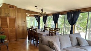 A spacious living area with a wooden floor, a grey sofa, a dining table with chairs, and large windows with curtains. - The Emerald Lake House (Lake Almanor)