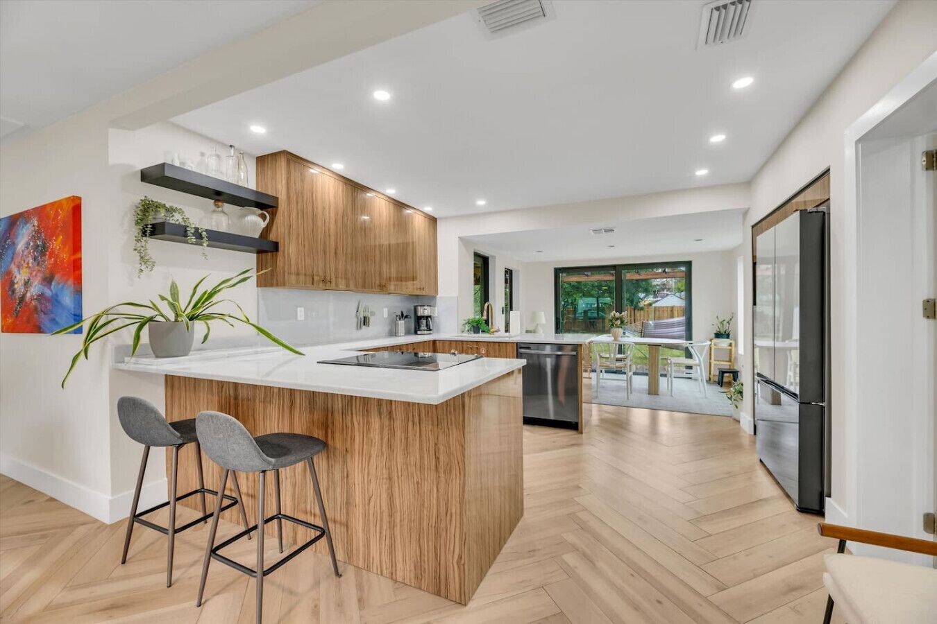 A modern kitchen with a central island, bar stools, wooden cabinets, and a view to a dining area.