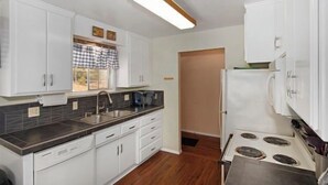 Una cocina con armarios blancos, encimera negra, pileta de acero inoxidable y refrigerador blanco.